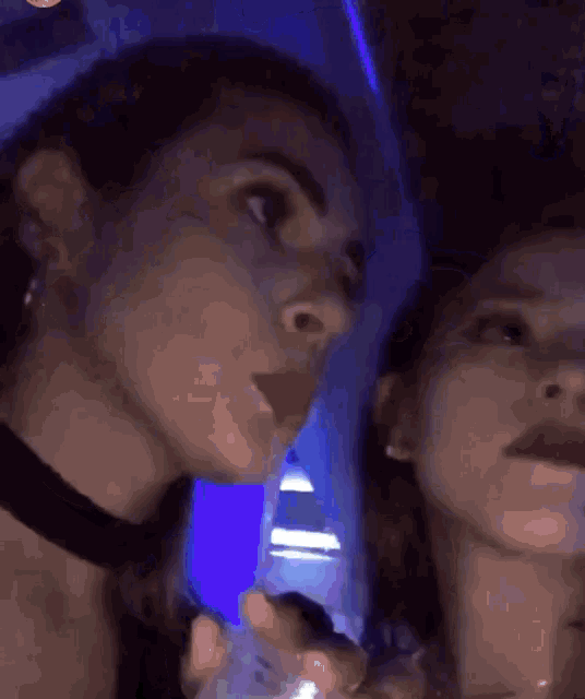 two women standing next to each other in a dark room with a blue light behind them