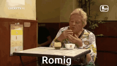 a woman sits at a table with a cup of coffee and says romig