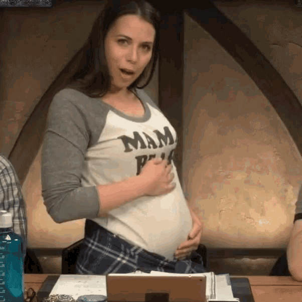 a pregnant woman holds her belly while wearing a mam pink shirt
