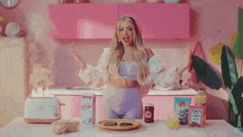 a woman is standing in a kitchen with her arms outstretched and a plate of food .