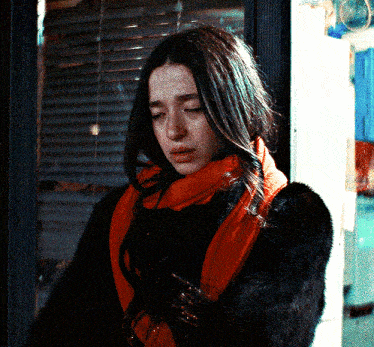a woman wearing a fur coat and an orange scarf looks down