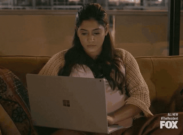 a woman is sitting on a couch using a laptop and the fox logo is visible