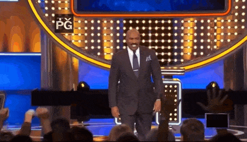 a man in a suit and tie stands on a stage with a pg sign in the background