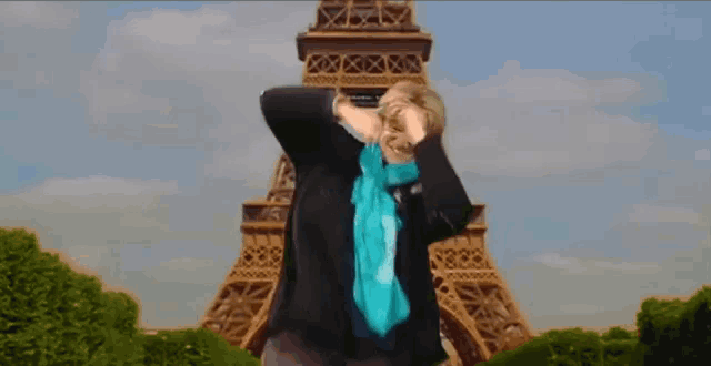 a woman wearing a blue scarf is standing in front of the eiffel tower