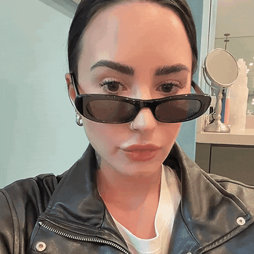 a woman wearing sunglasses and a leather jacket poses for a picture