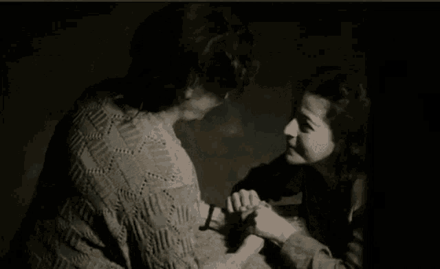 an elderly woman is smiling in a dark room while looking at another woman .