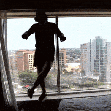 a man is jumping in the air in front of a window with a view of a city