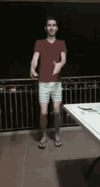 a man in striped shorts and flip flops stands on a balcony