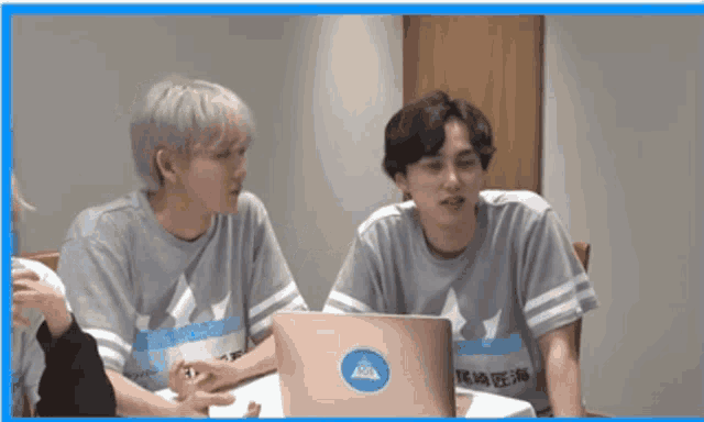 two young men are sitting at a table looking at a laptop with a sticker on it that says aaa