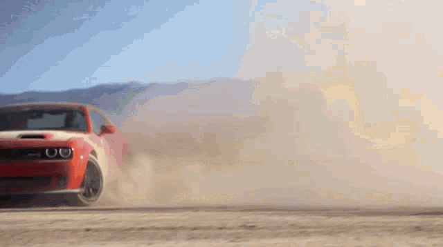 a red car is driving on a dirt road and kicking up dust