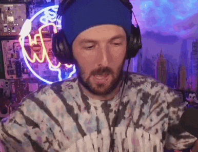 a man wearing headphones and a tie dye shirt is sitting in front of a neon sign .