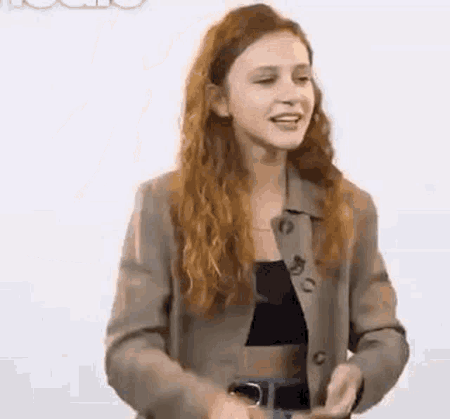 a young woman with long red hair is wearing a brown jacket and a black top .