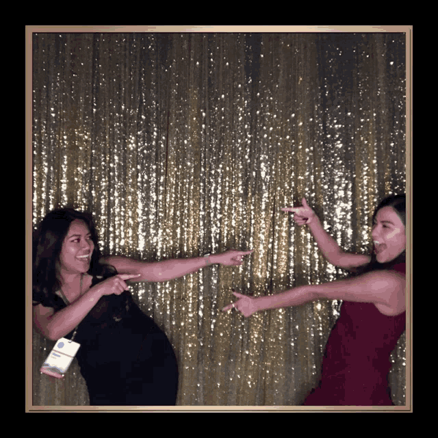 two women pose for a picture in front of a gold sequined wall