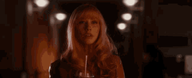 a woman with blonde hair and bangs looks at the camera in a dark room