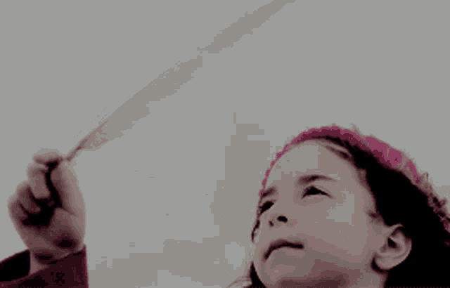 a little girl in a pink headband holds a feather in her hand