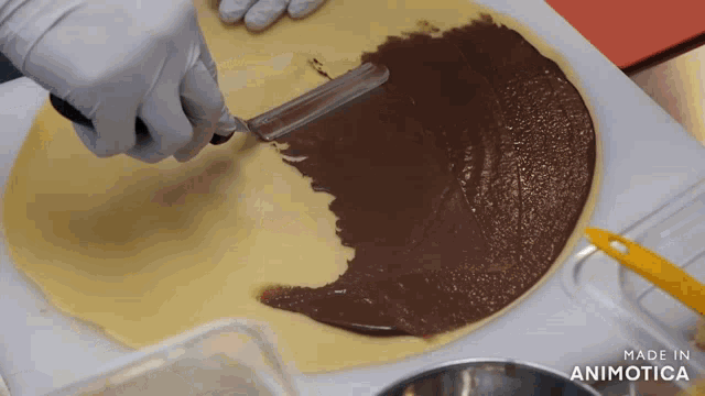 a person is spreading chocolate on a piece of dough and the words made in animotica can be seen in the background