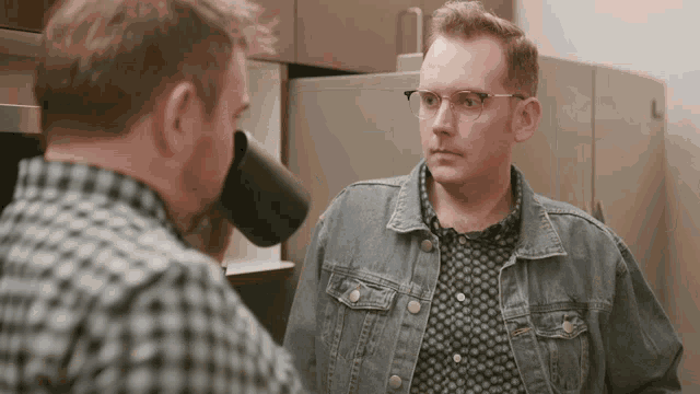 a man in a denim jacket is drinking from a black cup