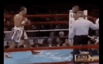 two men are boxing in a ring with a referee and a sign that says 2:30 on it .