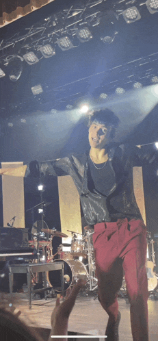 a man in a black jacket and red pants is standing on a stage