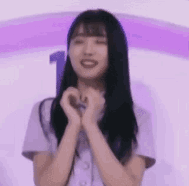 a woman with long black hair is making a heart with her hands .