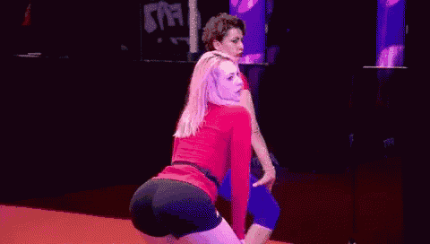 a woman in a red shirt and black shorts is dancing on a stage .