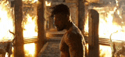 a man without a shirt is standing in front of a fire in a room .