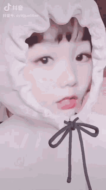 a girl wearing a white hoodie with a bow around her neck makes a funny face