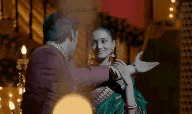 a man and a woman are dancing together and the woman is wearing a green saree