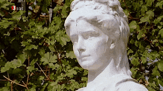 a statue of a woman is surrounded by green leaves and has the number 3 sat on it