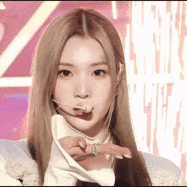 a woman with long blonde hair and a ring on her finger looks at the camera