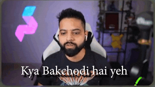 a man with a beard and headphones is sitting in a chair with the words kya bakchodi hai yeh on the screen .