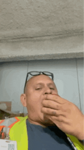 a man wearing glasses and a yellow vest is eating an apple