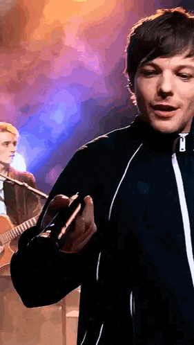 a man in a blue jacket is holding a guitar in front of a microphone on a stage .