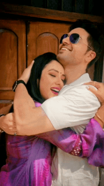 a man wearing sunglasses is hugging a woman wearing a purple dress