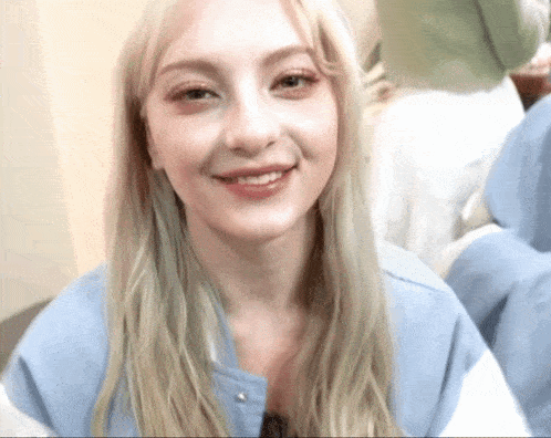 a woman with blonde hair is smiling and wearing a light blue jacket