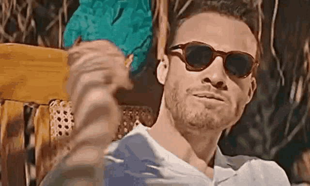 a man wearing sunglasses is sitting in a chair and making a funny face .