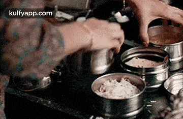 a person is cooking food in a metal container on a stove .