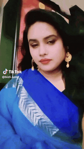 a woman wearing a blue saree and gold earrings has a tiktok icon on her face