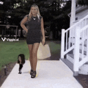 a woman in a black dress is walking down a sidewalk next to a white staircase