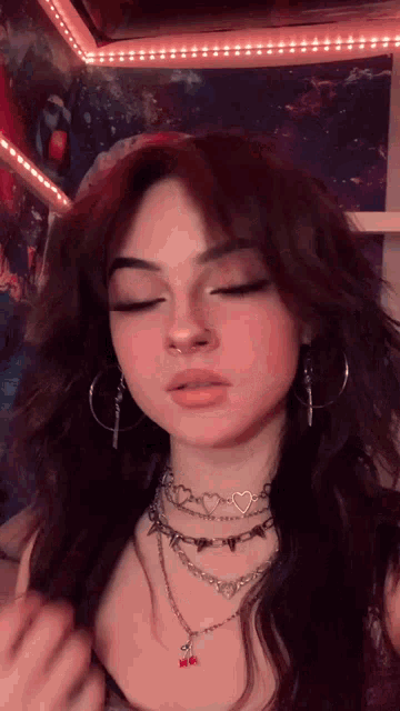 a girl with a nose ring is wearing a necklace and hoop earrings .