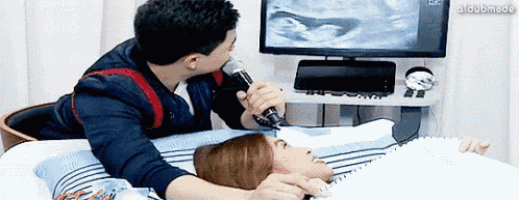 a man is singing into a microphone while a woman lays on a bed