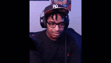 a man wearing headphones and a ny hat looks at the camera
