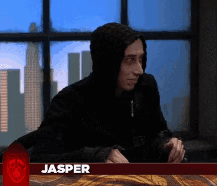 a man in a black hoodie is sitting at a table with the name jasper on the bottom