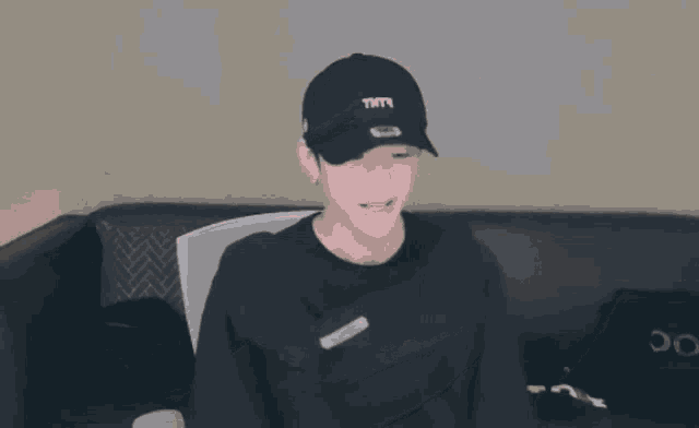 a man wearing a black hat and a black hoodie is laying down on a couch .