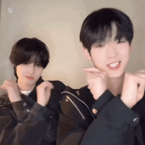 two young men are making a heart shape with their hands and smiling .