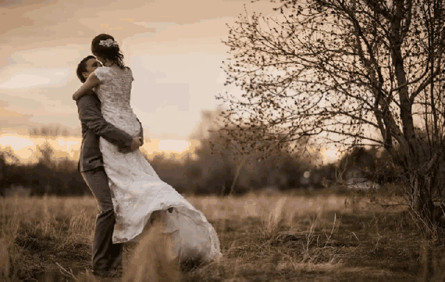 a bride and groom hugging in a field with trees in the background