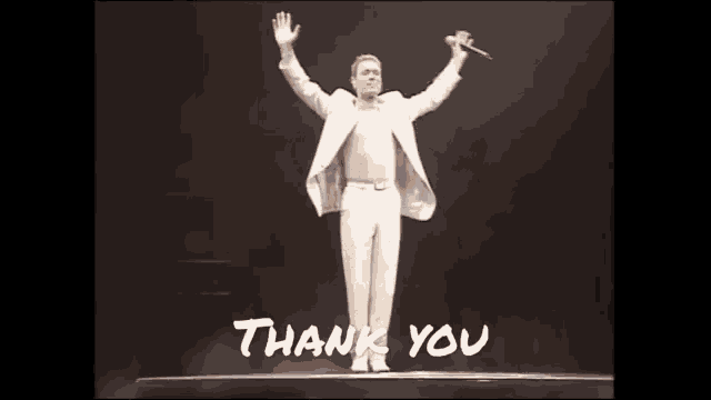 a man in a white suit is standing on a stage with his arms outstretched and a microphone in his hand .