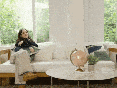 a woman sits on a couch in front of a globe on a table