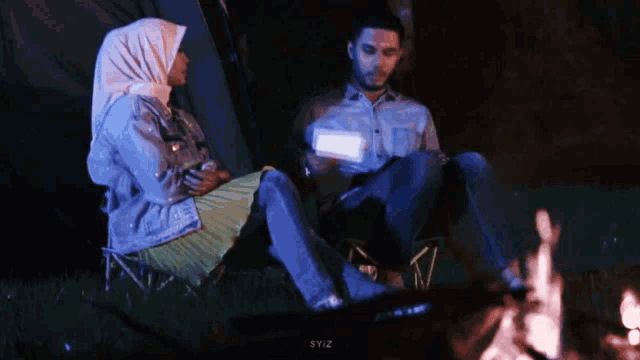 a man and a woman sit in front of a campfire with syiz written in the corner