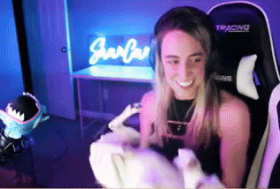 a woman wearing headphones is sitting in a gaming chair holding a stuffed animal and smiling .